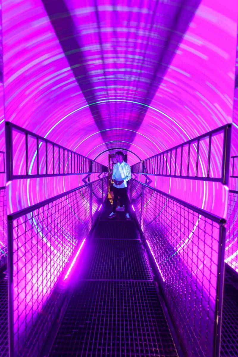 a person walking down a tunnel with purple lights