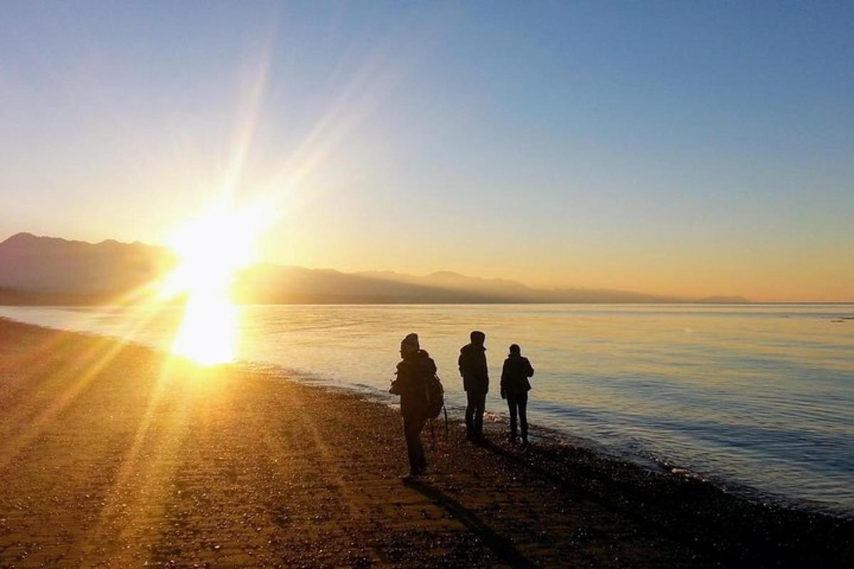 Tres personas paradas en la playa viendo la puesta de sol