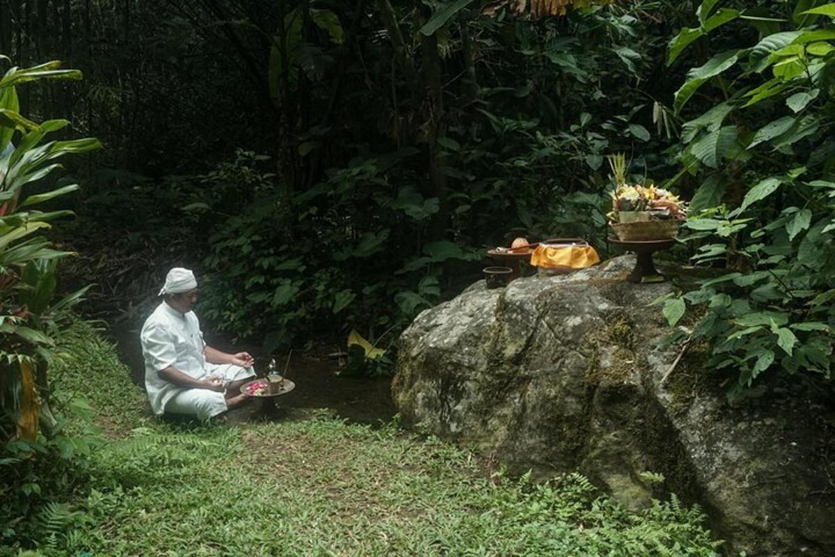 a man sitting on the grass next to a rock