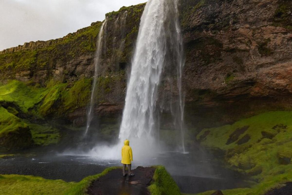 Maður í gulum jakka stendur fyrir framan foss
