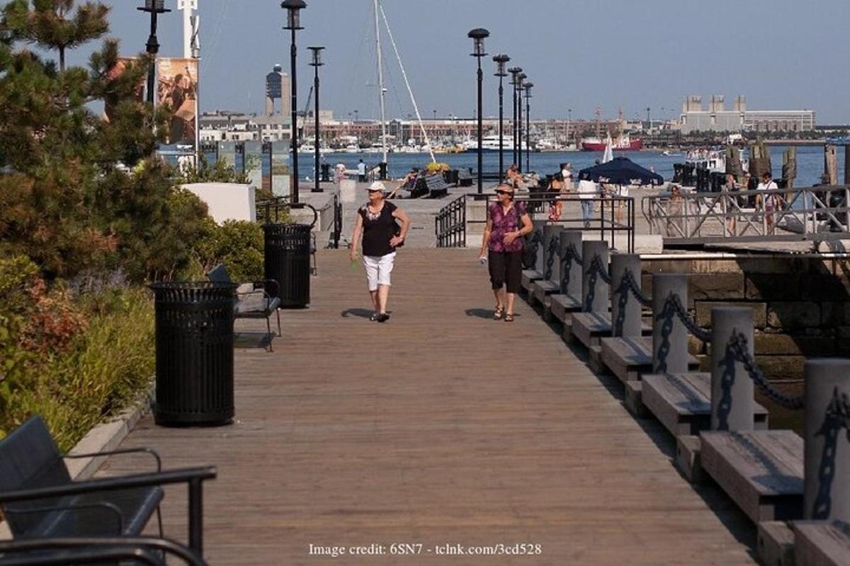 two people walking down a boardwalk near a harbor