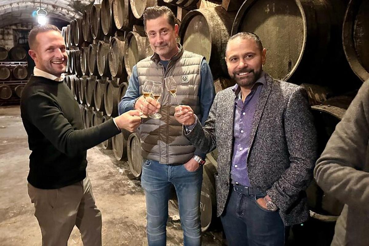 tři muži stojící ve vinném sklepě a držící sklenice na víno
