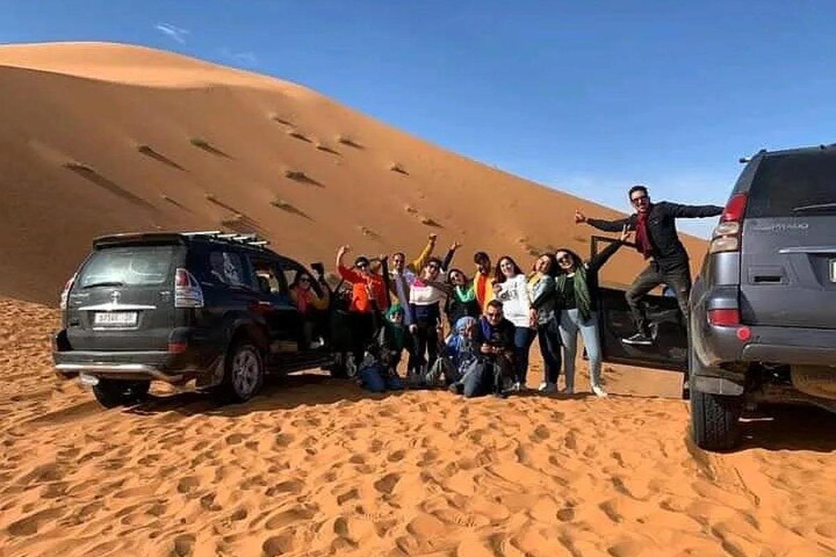 um grupo de pessoas em pé em frente a uma duna de areia