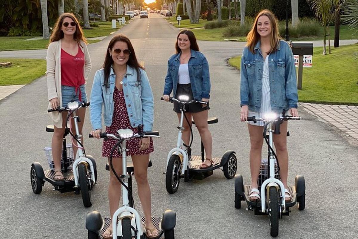 a group of four girls riding scooters down a street