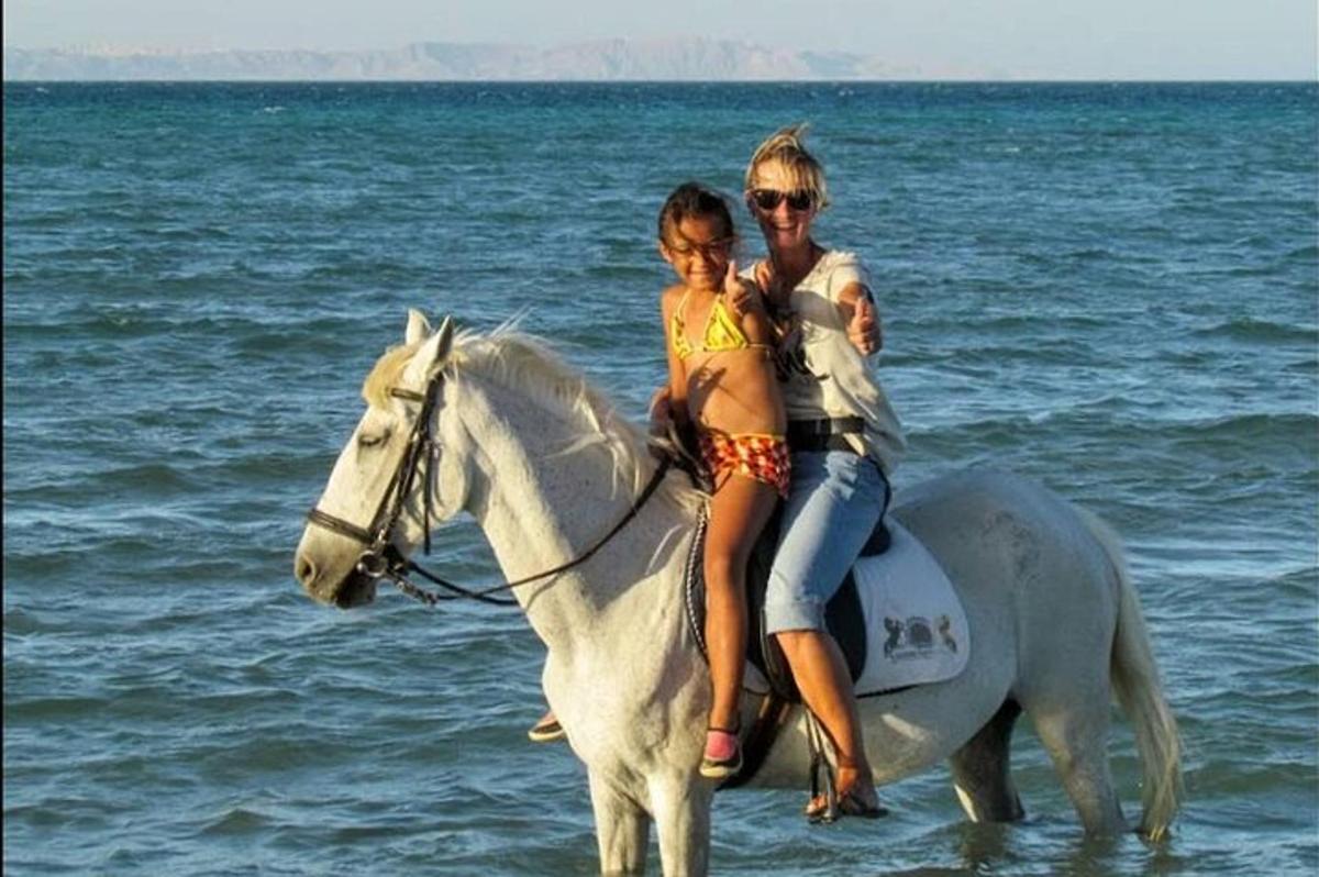 uma mulher e uma menina cavalgando na praia