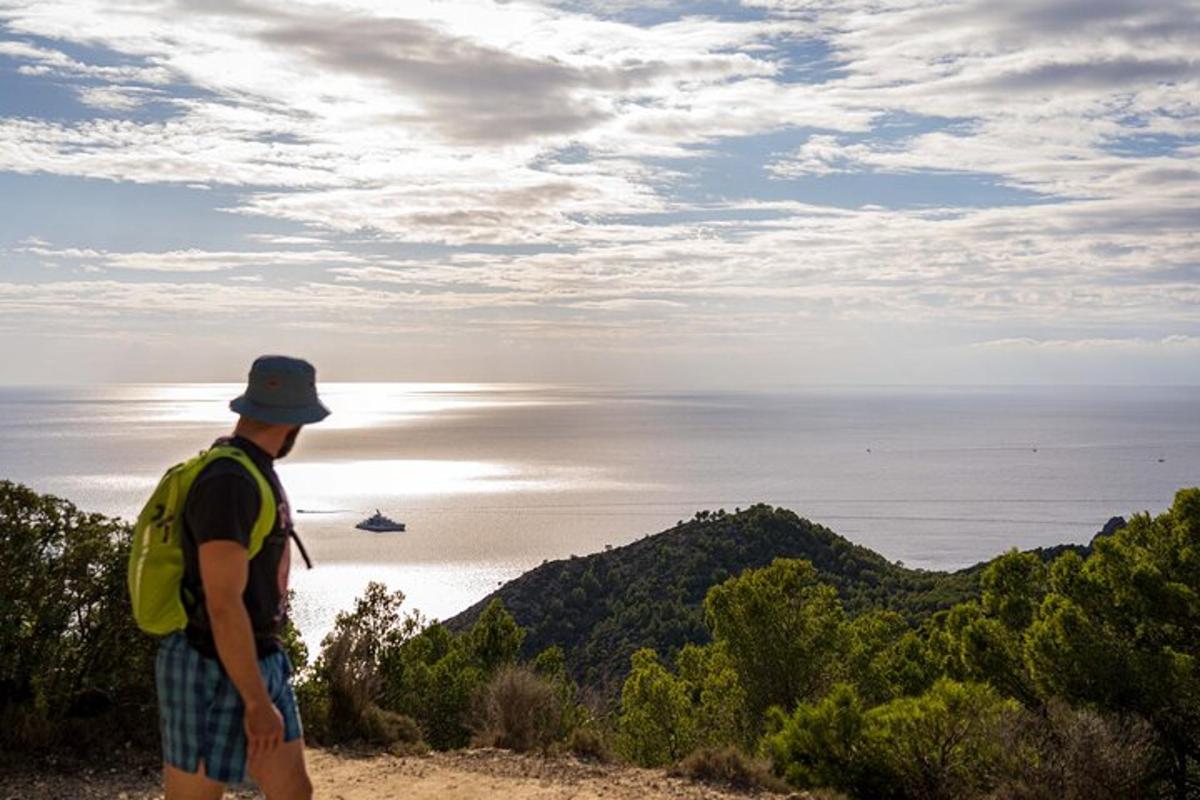 a man with a backpack standing on a hill looking at the ocean