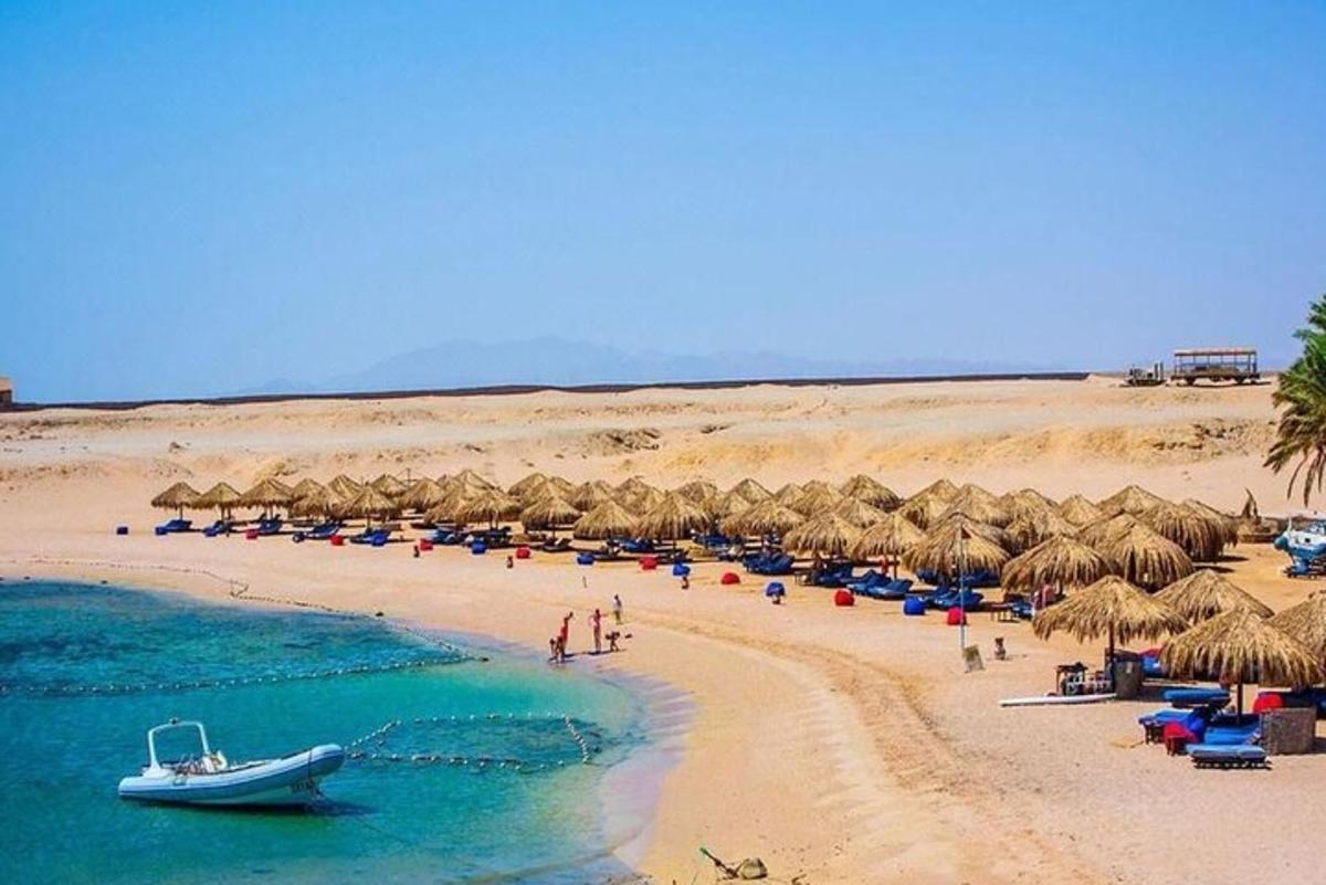 Una playa con sombrillas de paja y un barco en ella.