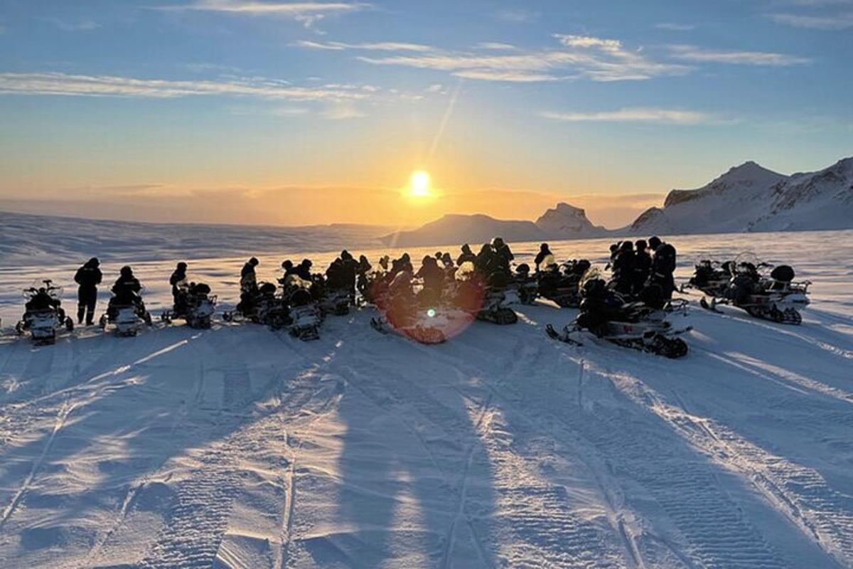 en gruppe mennesker sidder i sneen ved solnedgang