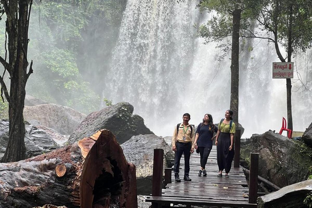 três pessoas em pé em uma ponte em frente a uma cachoeira
