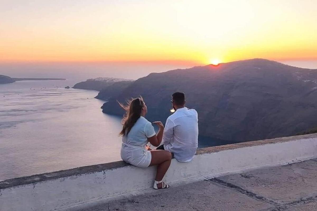 một người đàn ông và một người phụ nữ ngồi trên mỏm đá ngắm hoàng hôn