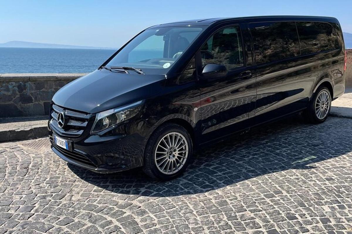 uma van preta estacionada em uma estrada de tijolos ao lado do oceano