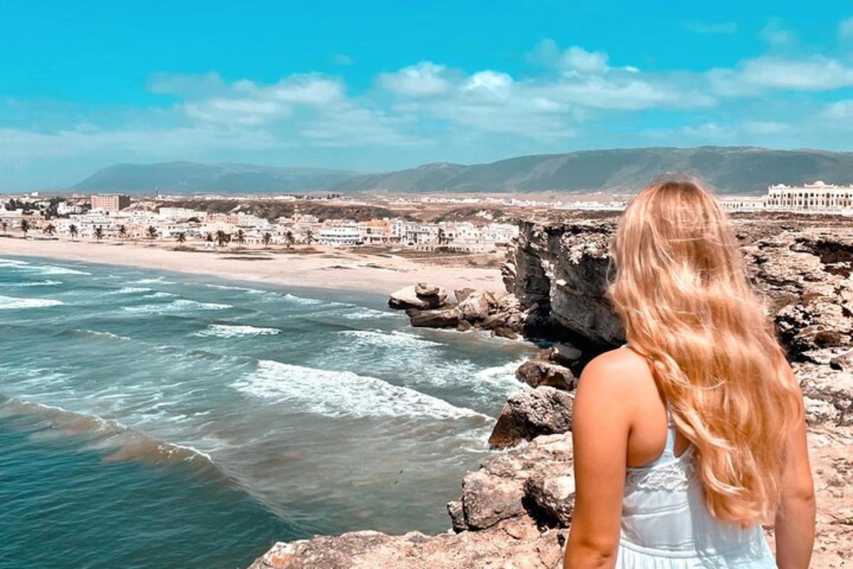 a woman standing on the rocks looking at the ocean