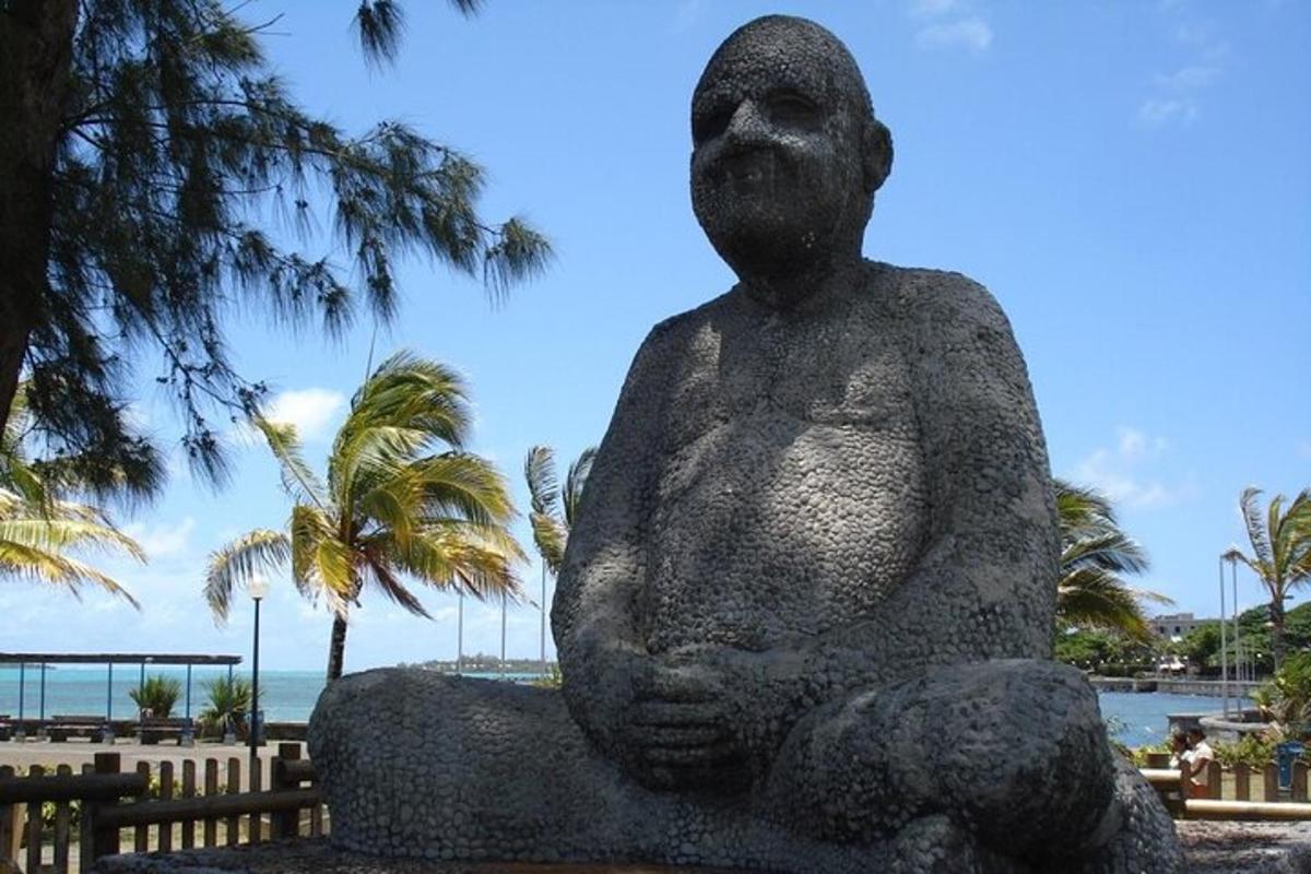 a statue of a man sitting on a rock next to the beach