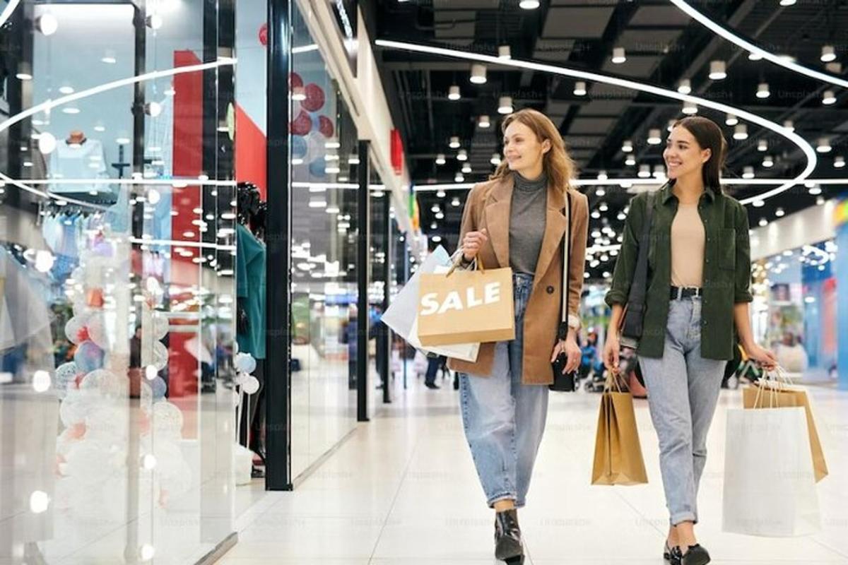 hai người phụ nữ đang đi dọc lối đi trong cửa hàng với những chiếc túi mua sắm