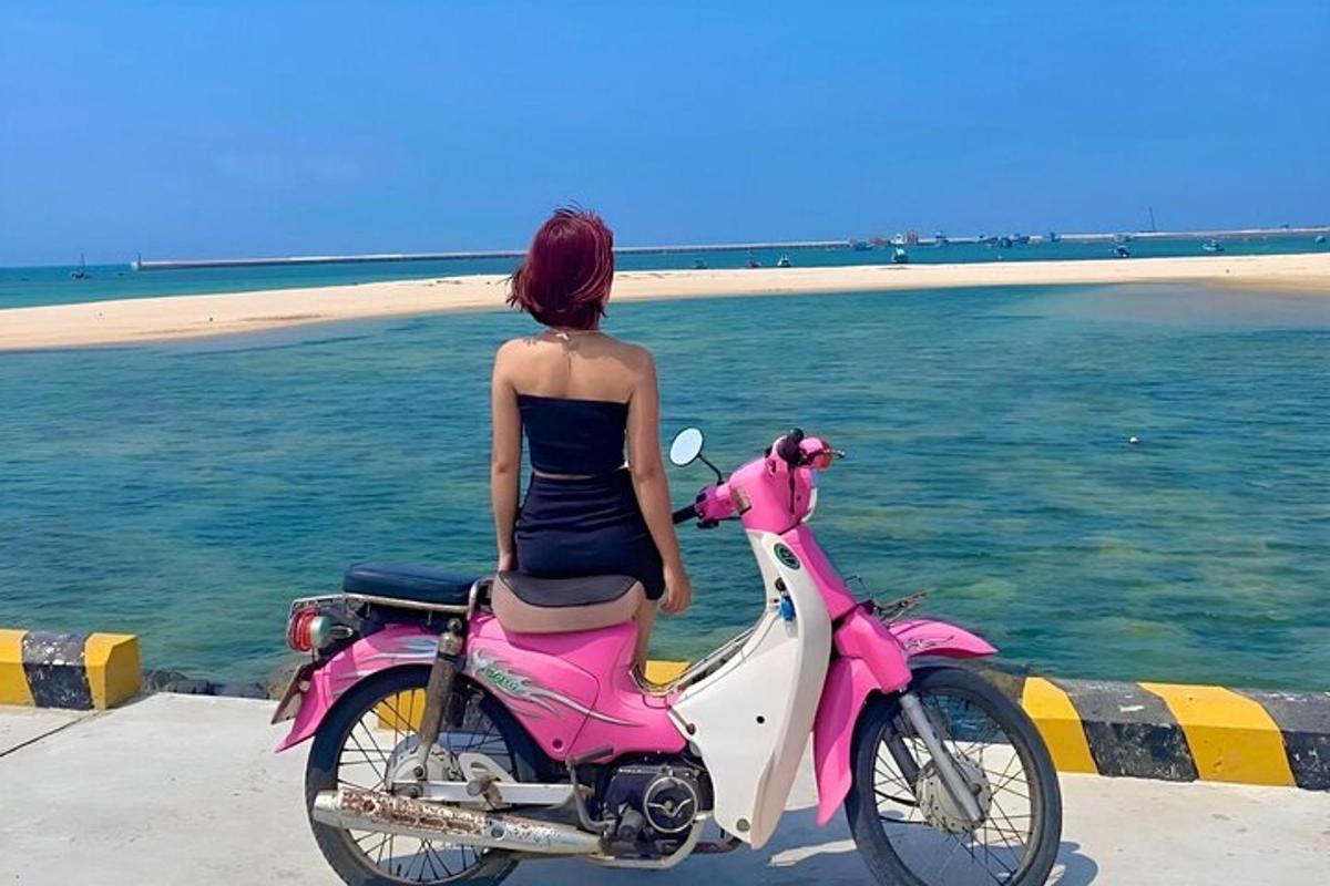 una dona asseguda en una motocicleta rosa al costat de l'oceà