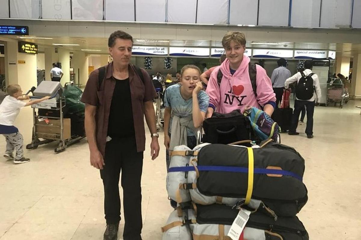 two men and a girl pushing a luggage cart at an airport