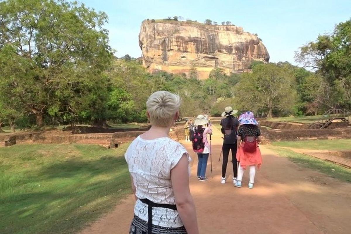 a group of people walking down a dirt road towards a rock