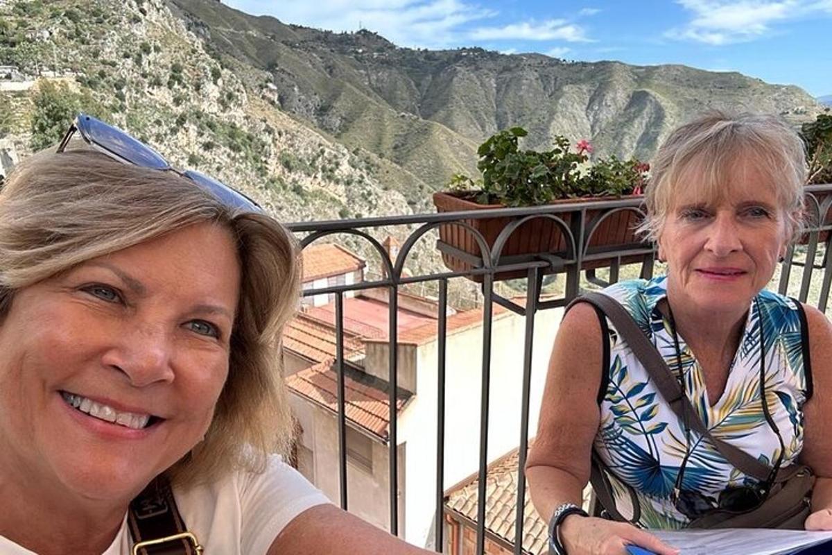 duas mulheres sentadas em uma varanda com montanhas ao fundo