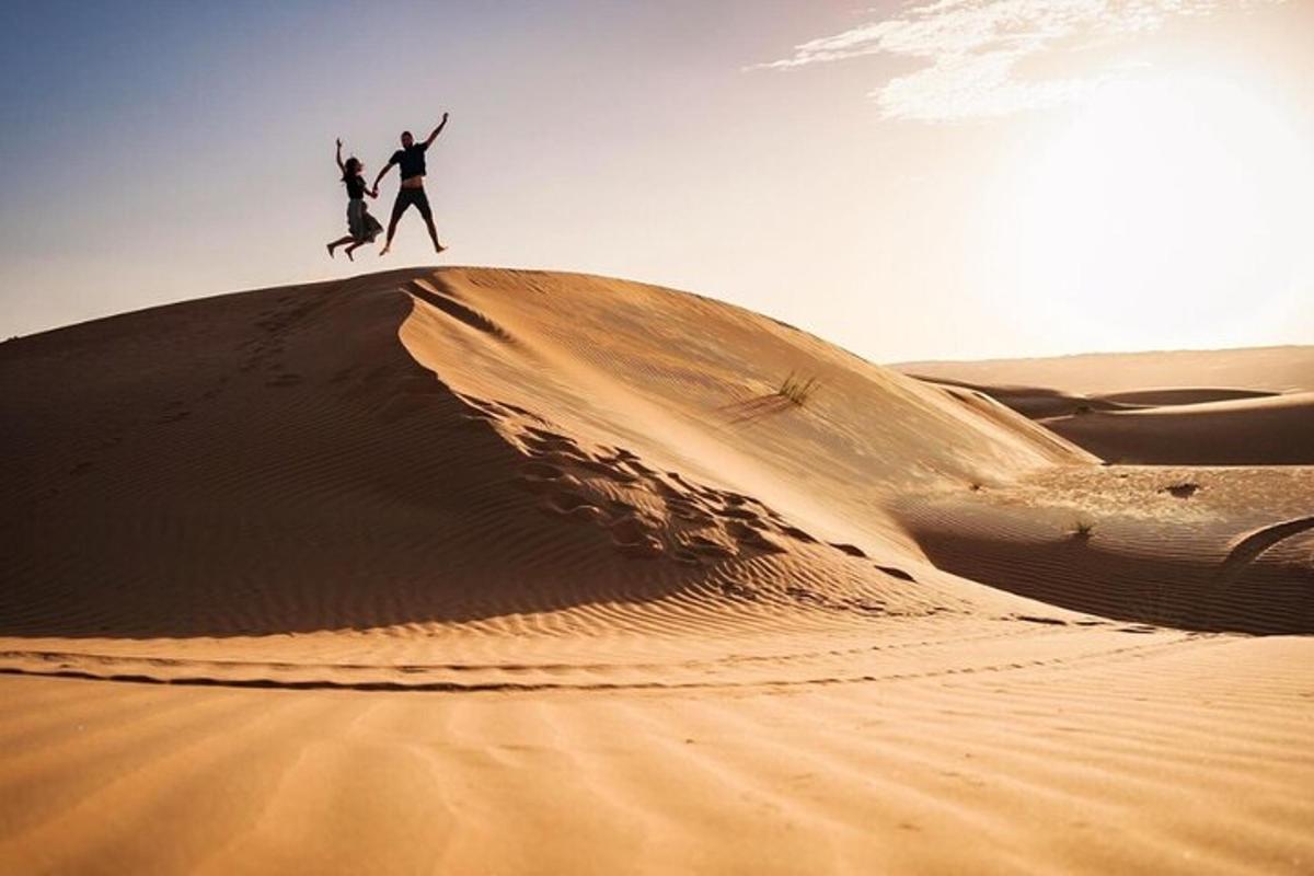 two people jumping off a sand dune in the desert