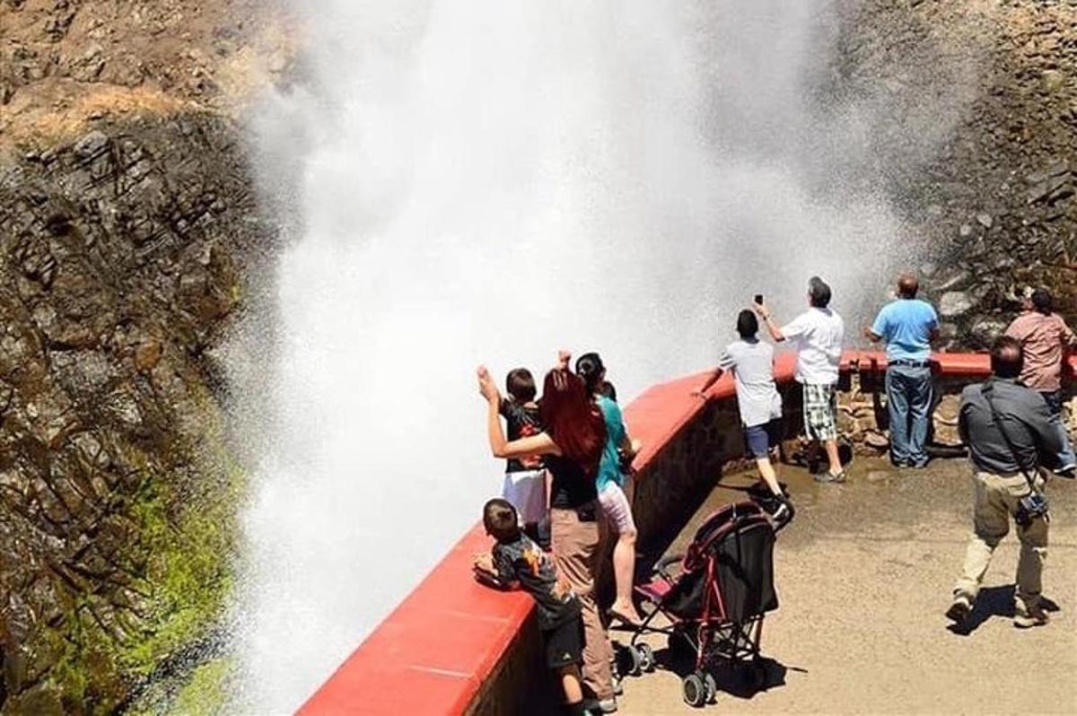 a group of people standing on a red bridge with a waterfall