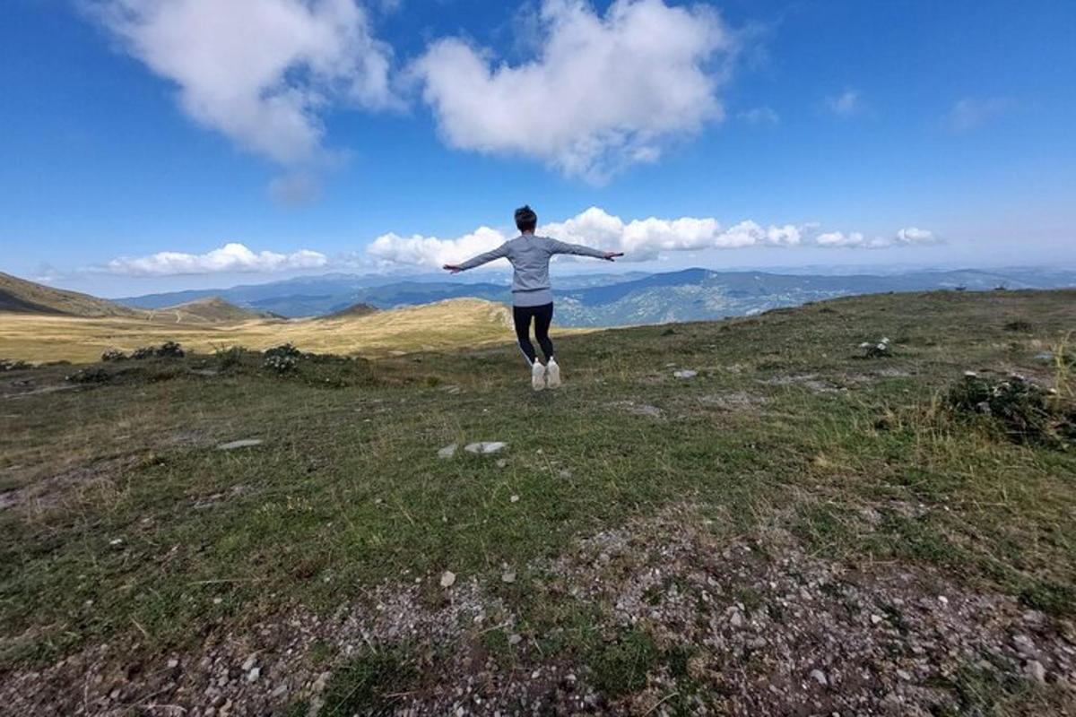una persona in piedi in cima a una collina con le braccia tese