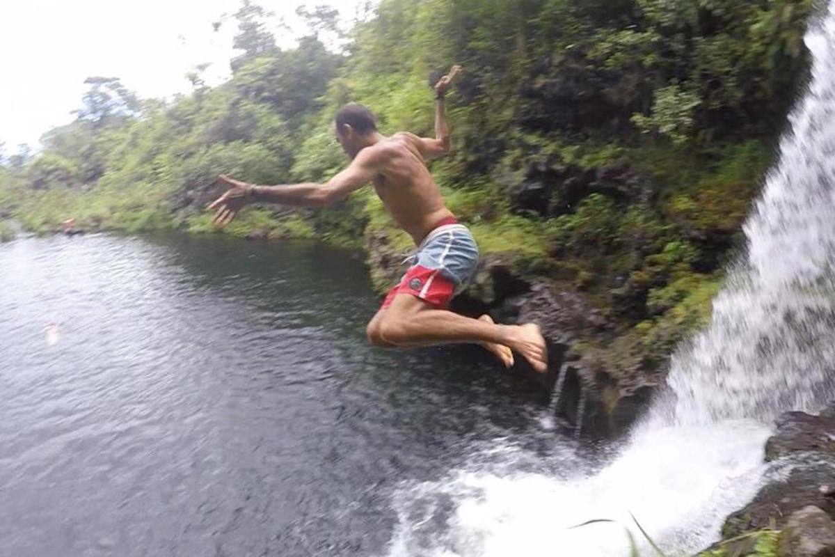 Un hombre saltando de una cascada a un cuerpo de agua.