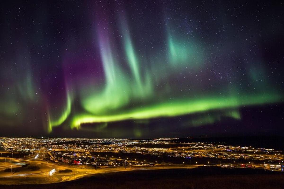 Norðurljós yfir borg að nóttu til með ljósum