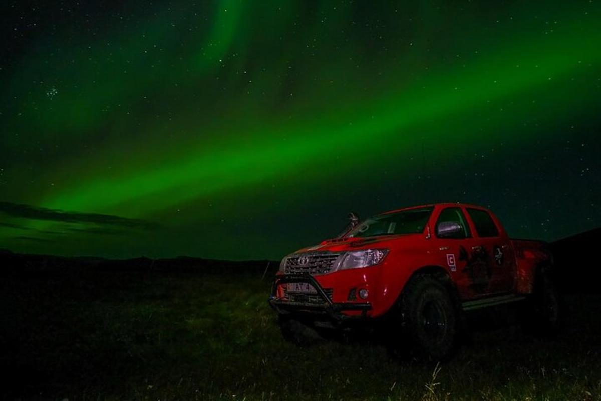 Rauður vörubíll lagður á akri undir norðurljósunum