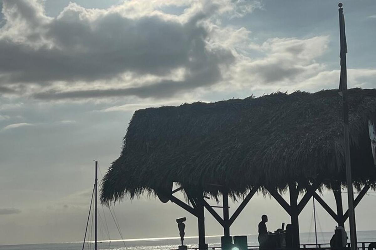 Una choza de paja con gente parada debajo de ella en la playa.