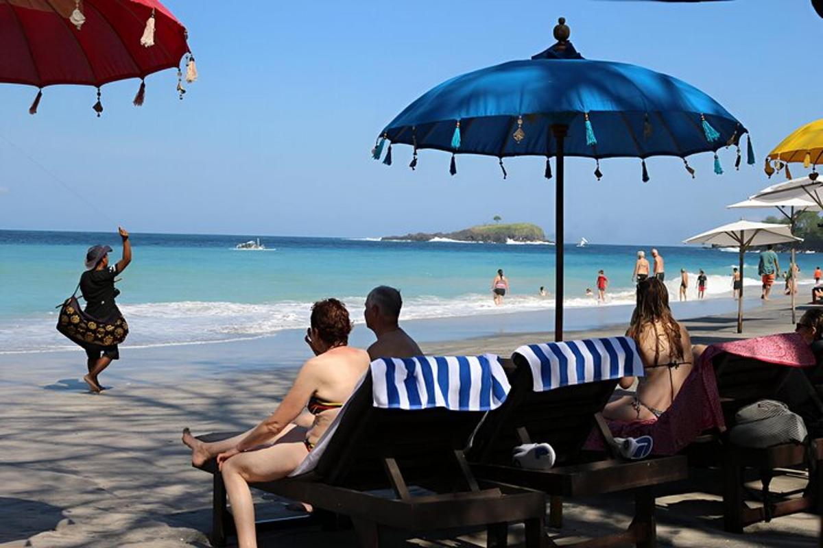 un grup de persones assegudes a la platja sota un para-sol