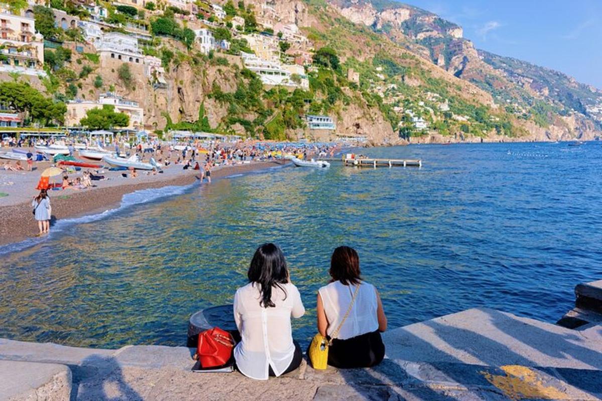 duas mulheres sentadas em uma saliência com vista para uma praia