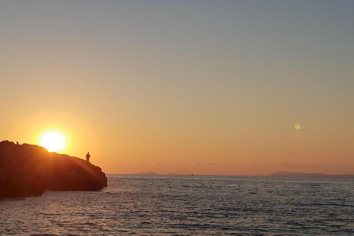 oseba, ki stoji na skali v oceanu ob sončnem zahodu