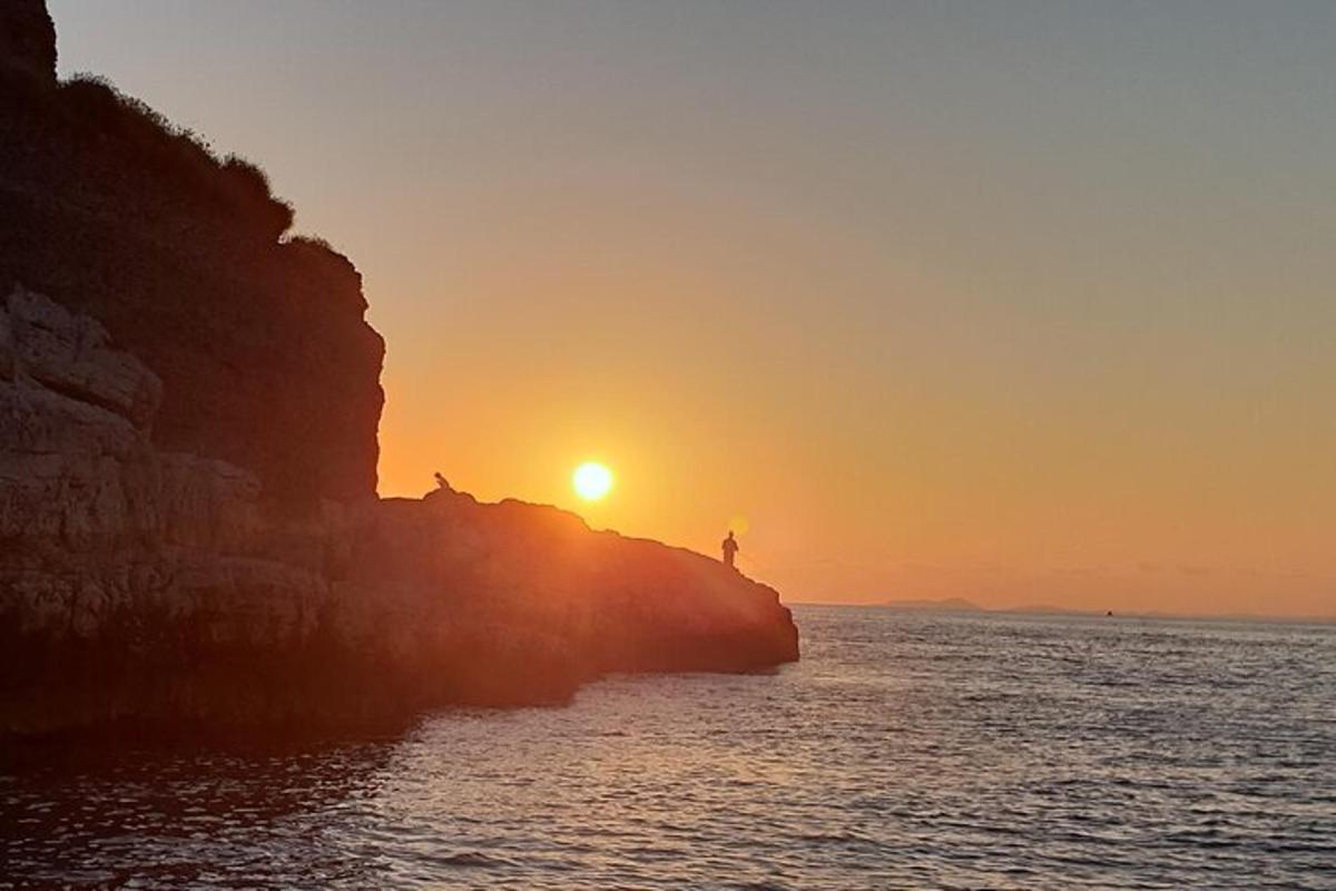 sončni zahod nad oceanom z osebo, ki stoji na pečini