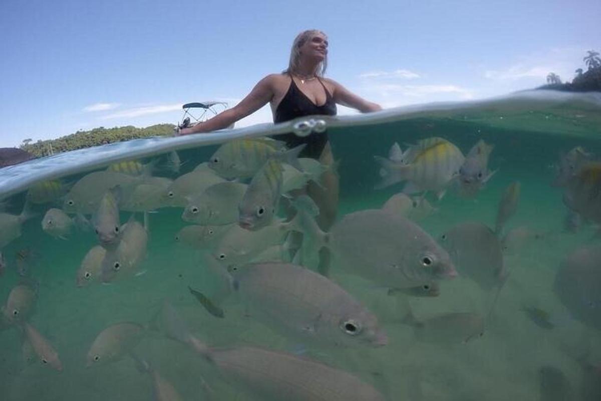 une femme tenant une planche de surf dans l'eau avec un troupeau de poissons