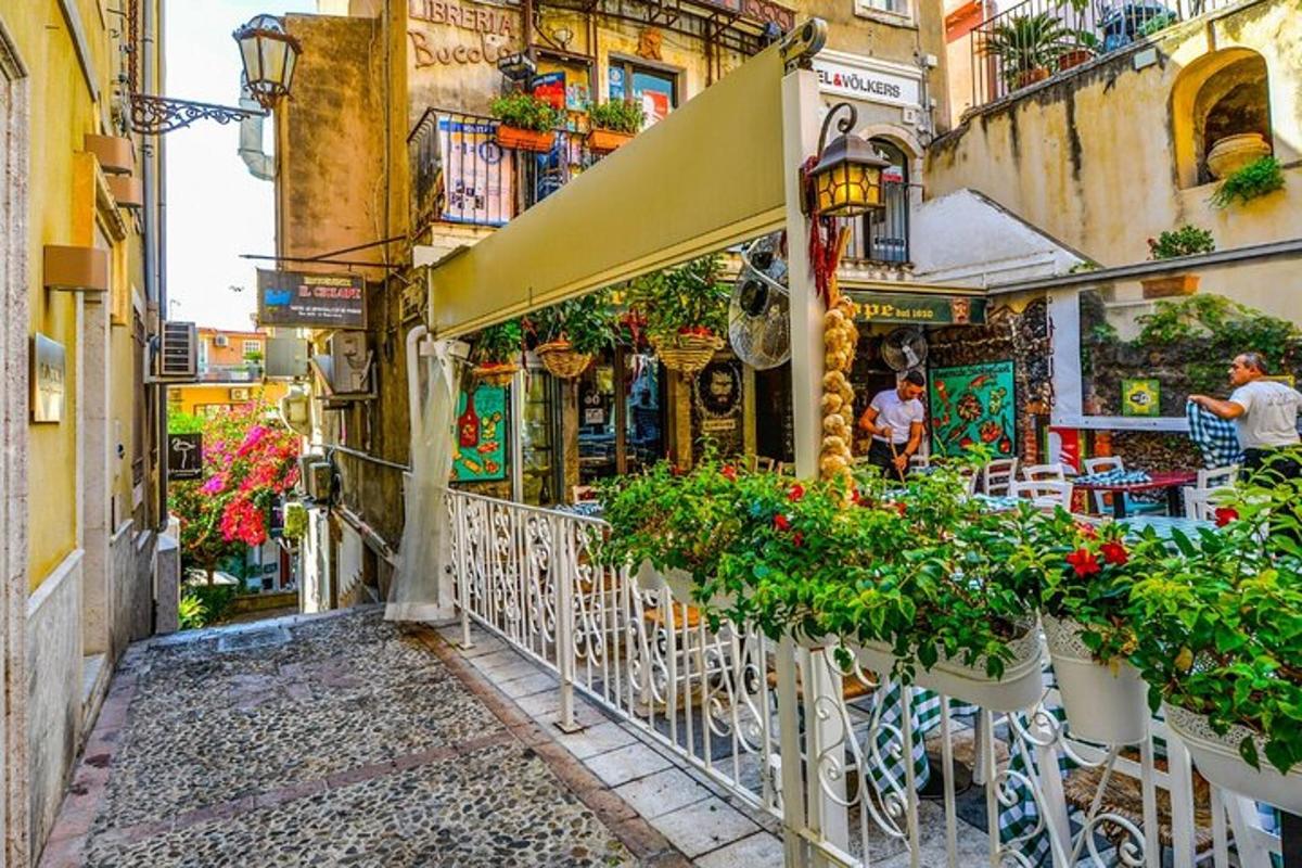 Un callejón con mesas y sillas y flores en un edificio.