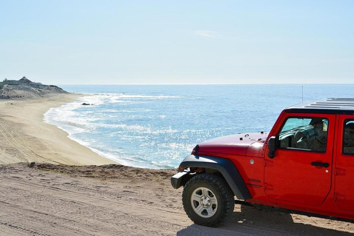 um caminhão vermelho estacionado em uma praia perto do oceano
