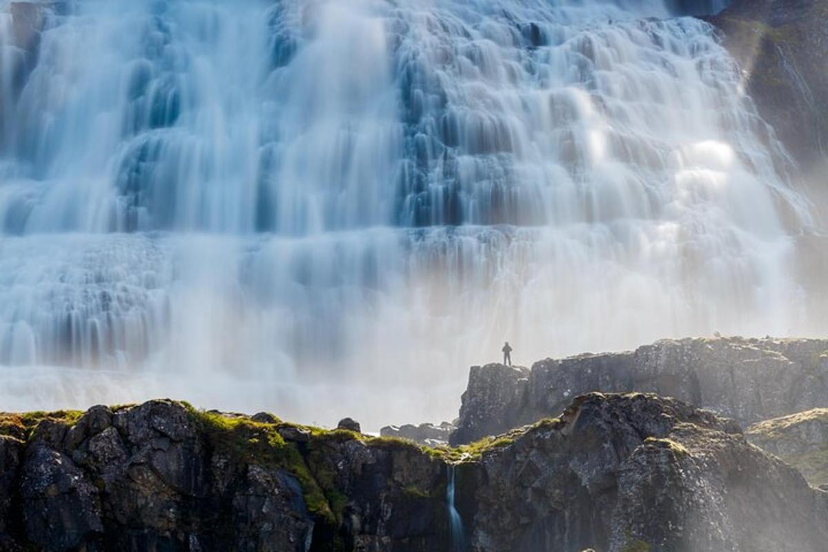 a person standing on a rock in front of a waterfall