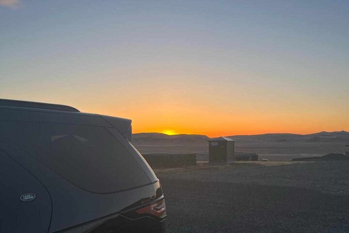 Un coche aparcado frente a una puesta de sol en el desierto.