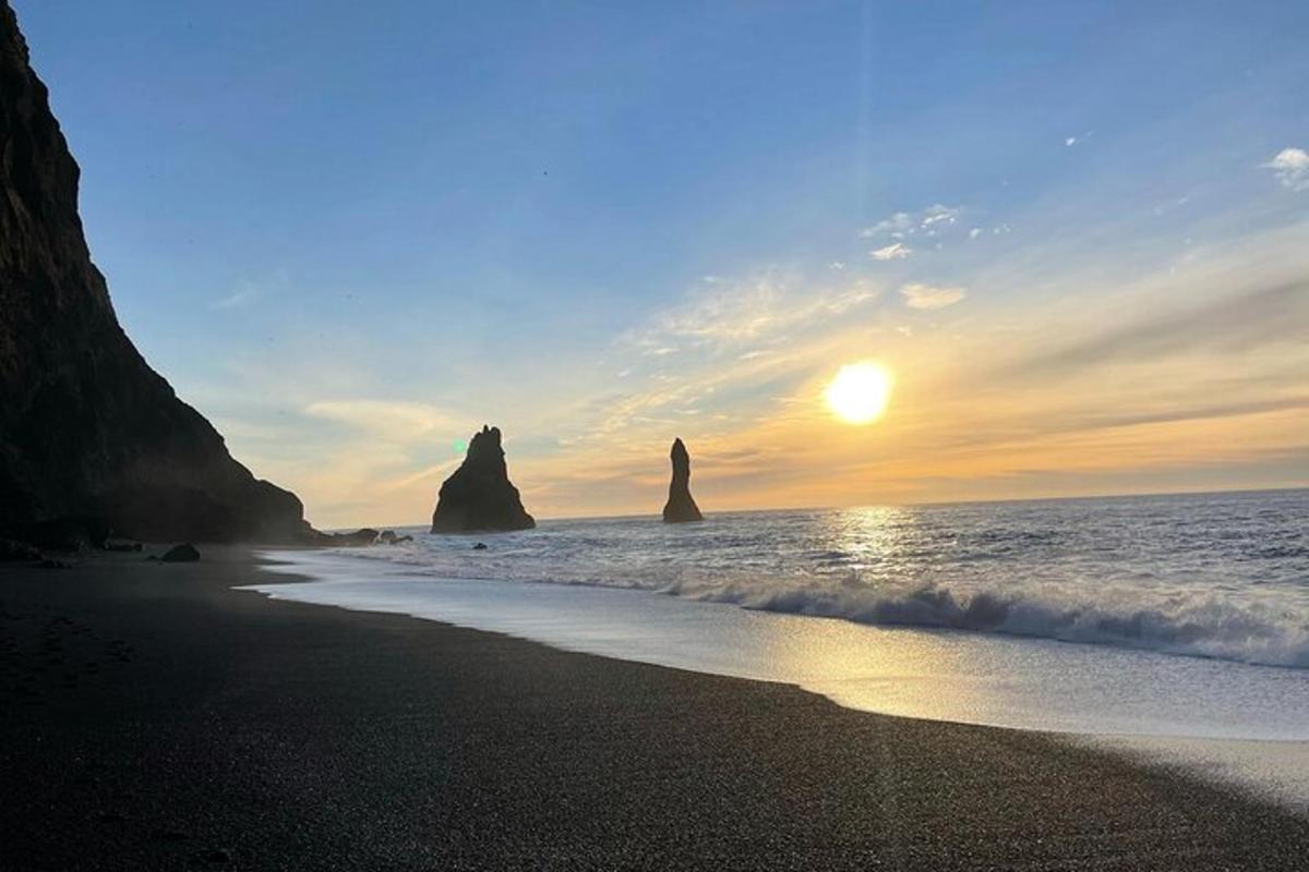 Una puesta de sol en una playa con dos grandes rocas en el agua.
