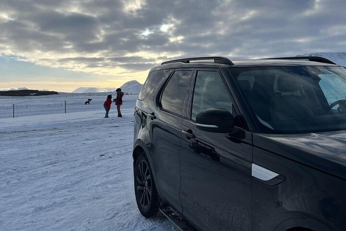 Un coche aparcado en una playa cubierta de nieve con gente al fondo.
