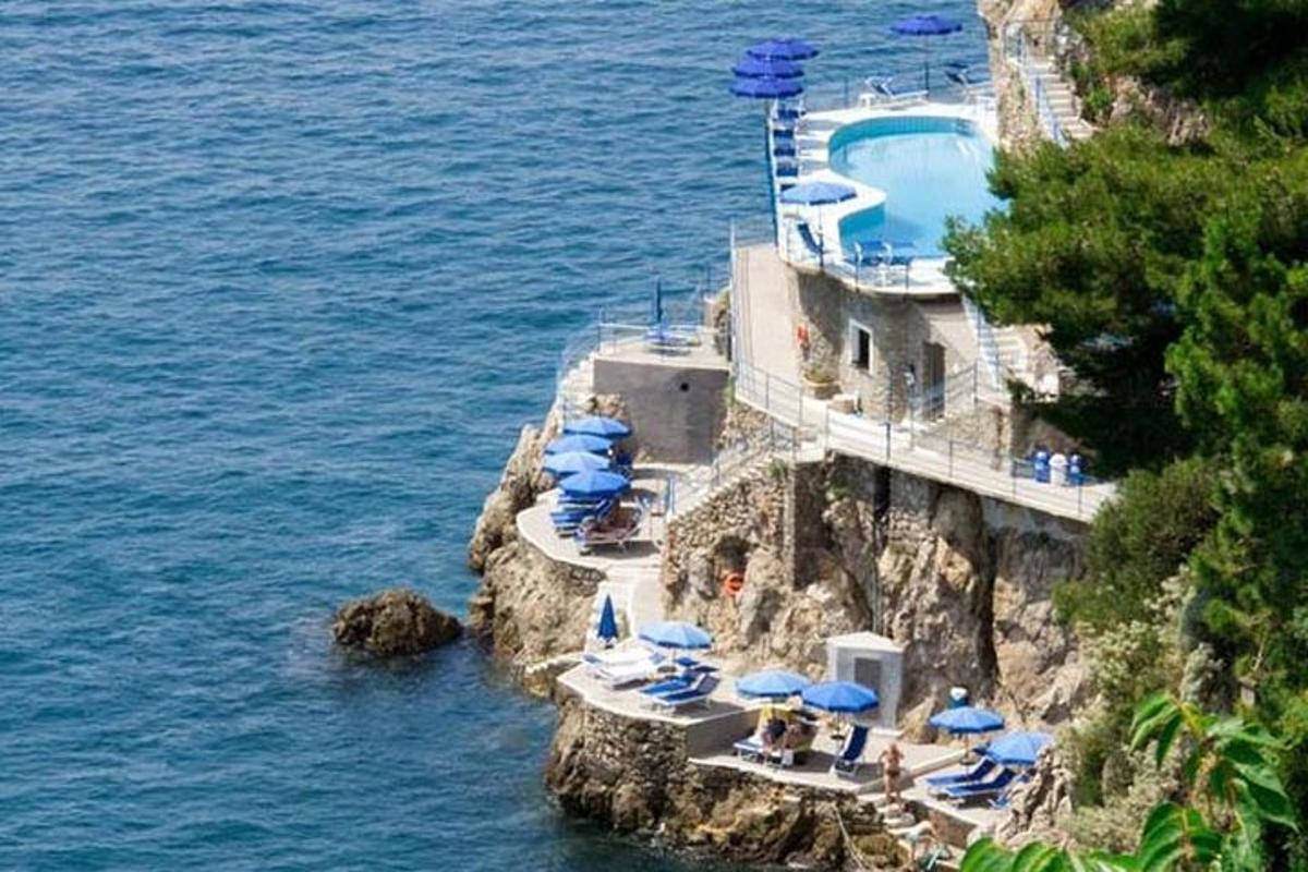 un edificio con ombrelloni blu e una piscina su una scogliera