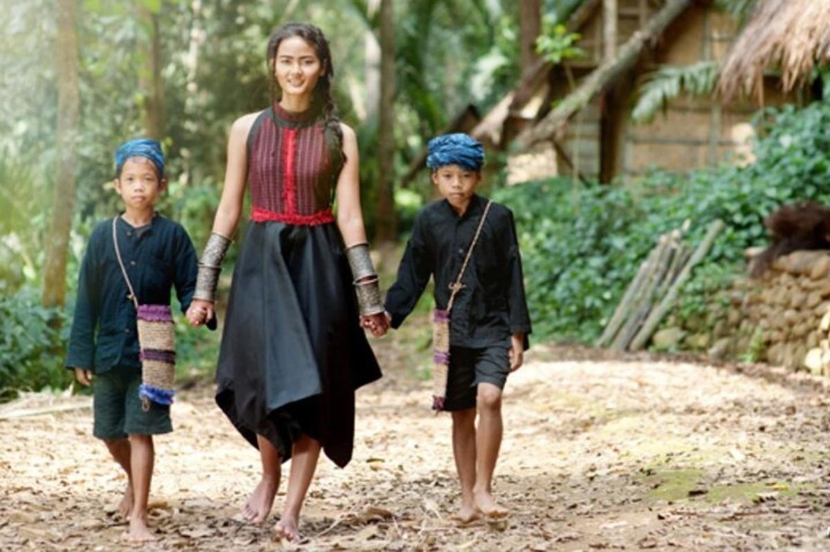 uma mulher e duas crianças caminhando por uma estrada de terra