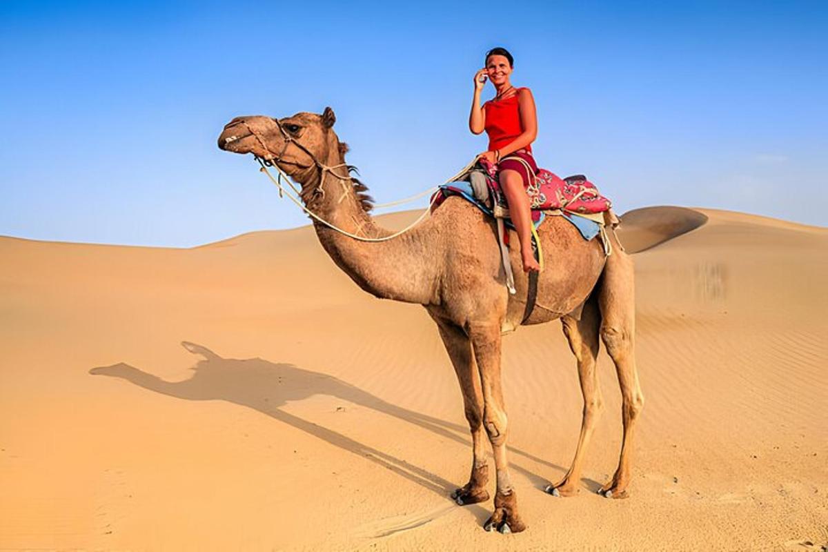 una dona muntant un camell al desert mentre parla per telèfon mòbil