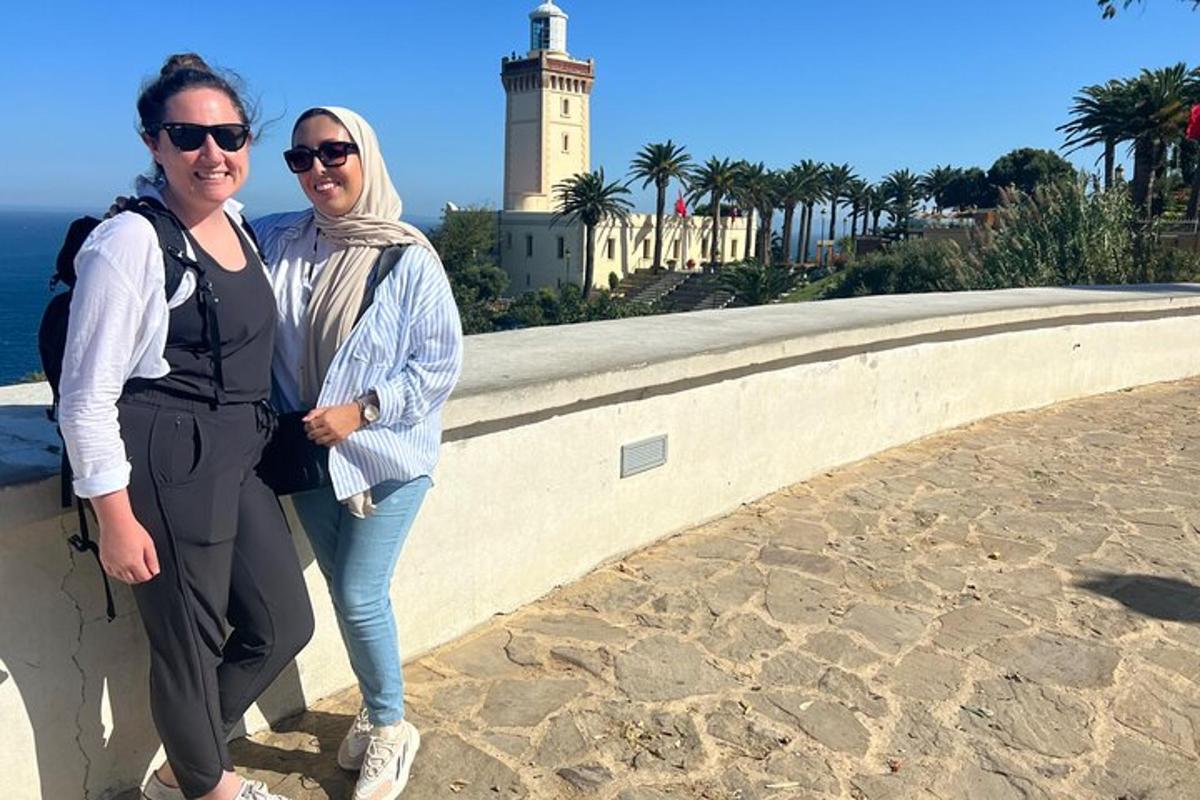Dos mujeres de pie junto a un muro con un faro.