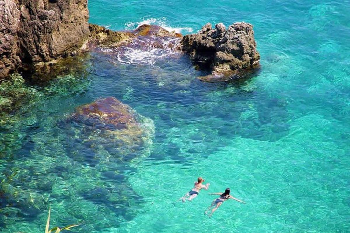 two people swimming in the water near some rocks