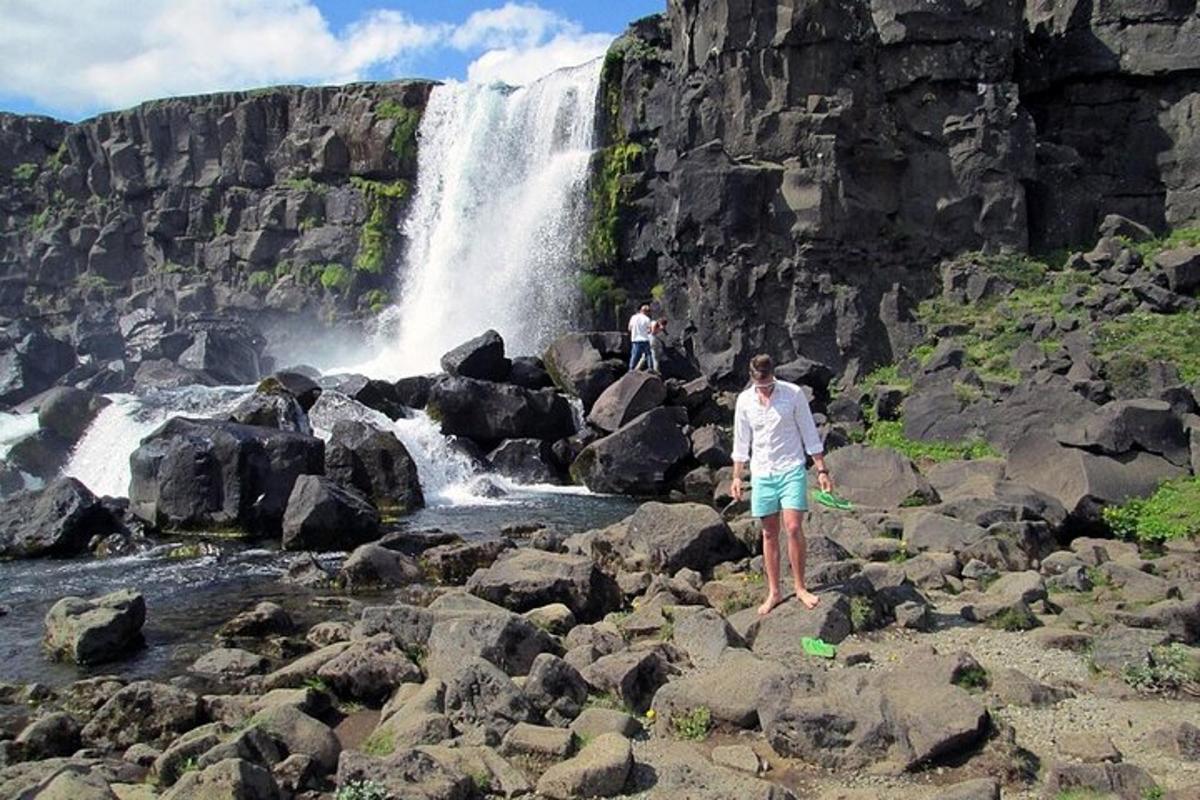 Un hombre parado sobre rocas frente a una cascada.