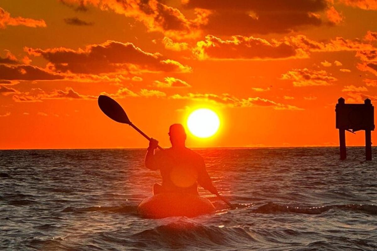 Un hombre está remando en un kayak en el océano al atardecer.
