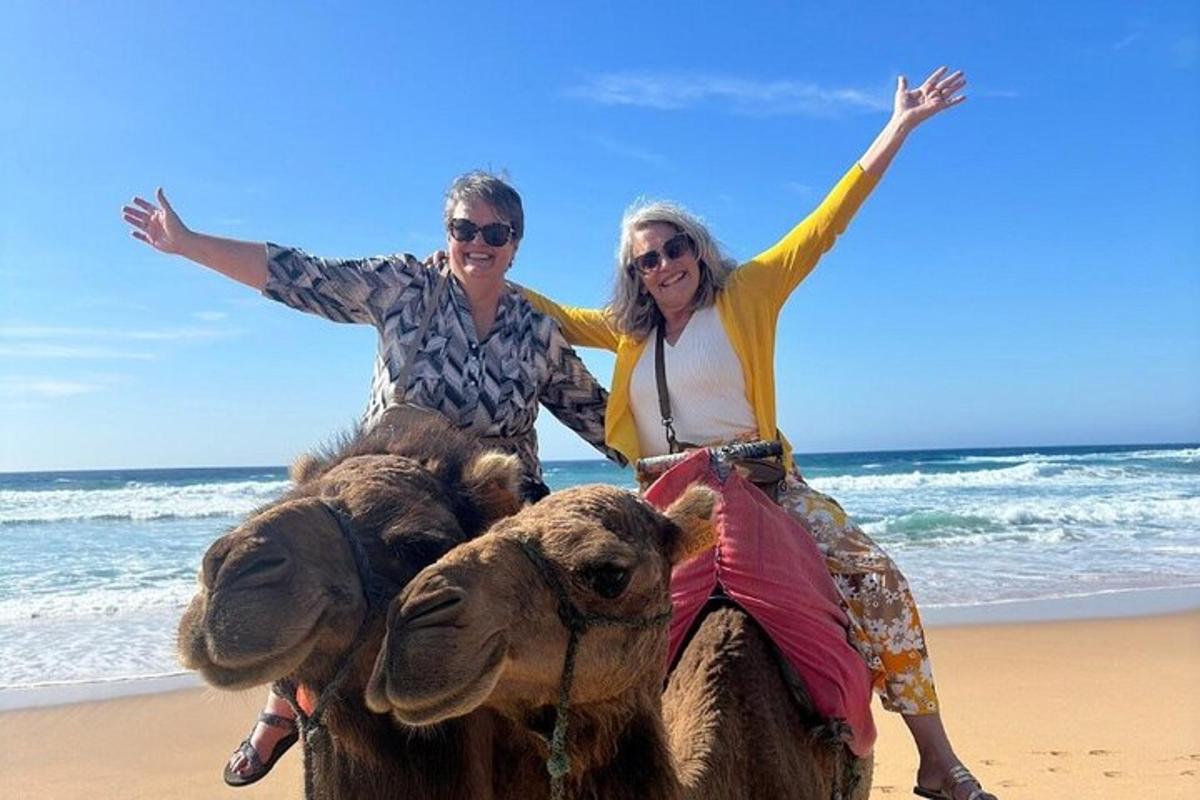 two people riding on a camel on the beach