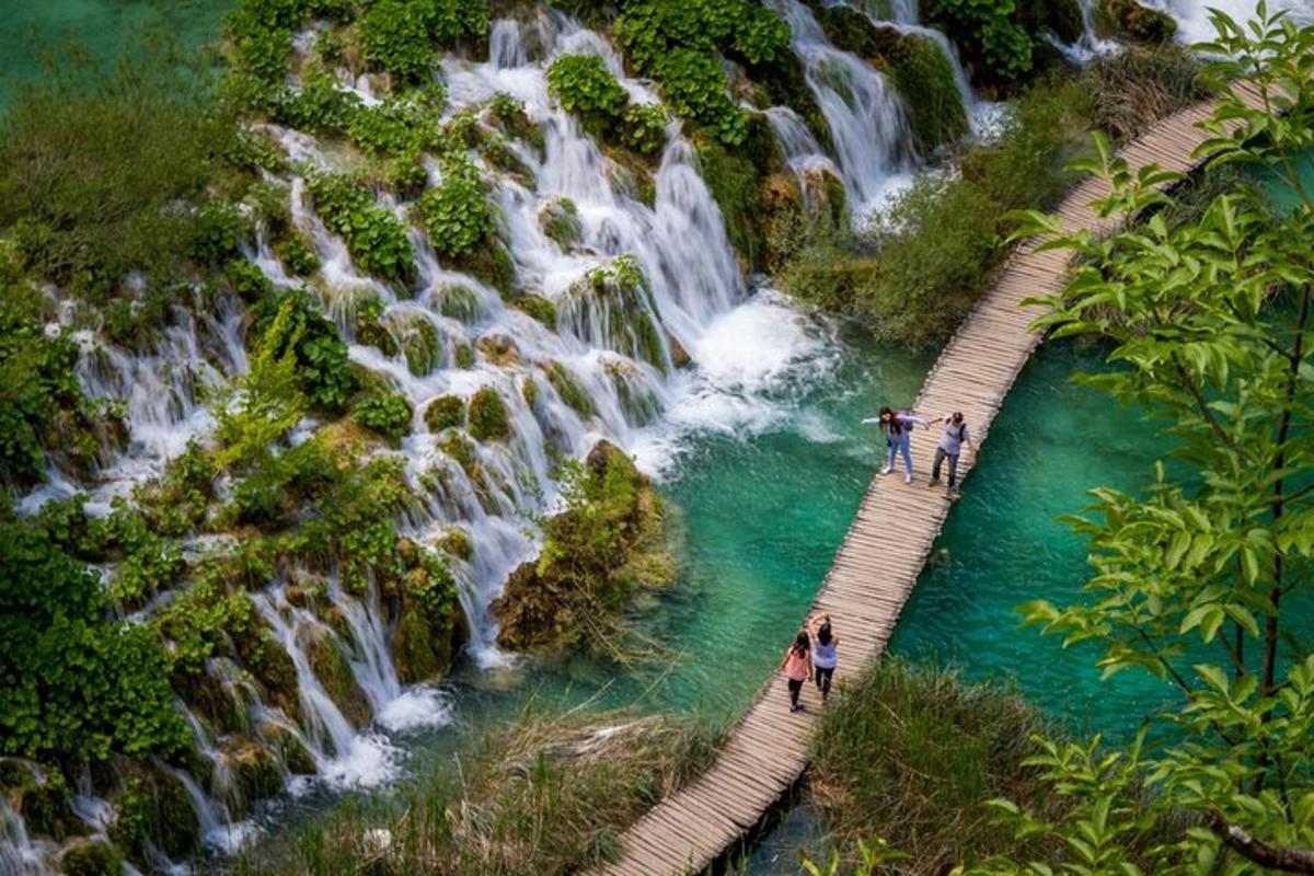 sekumpulan orang berdiri di atas jambatan kayu di atas air terjun
