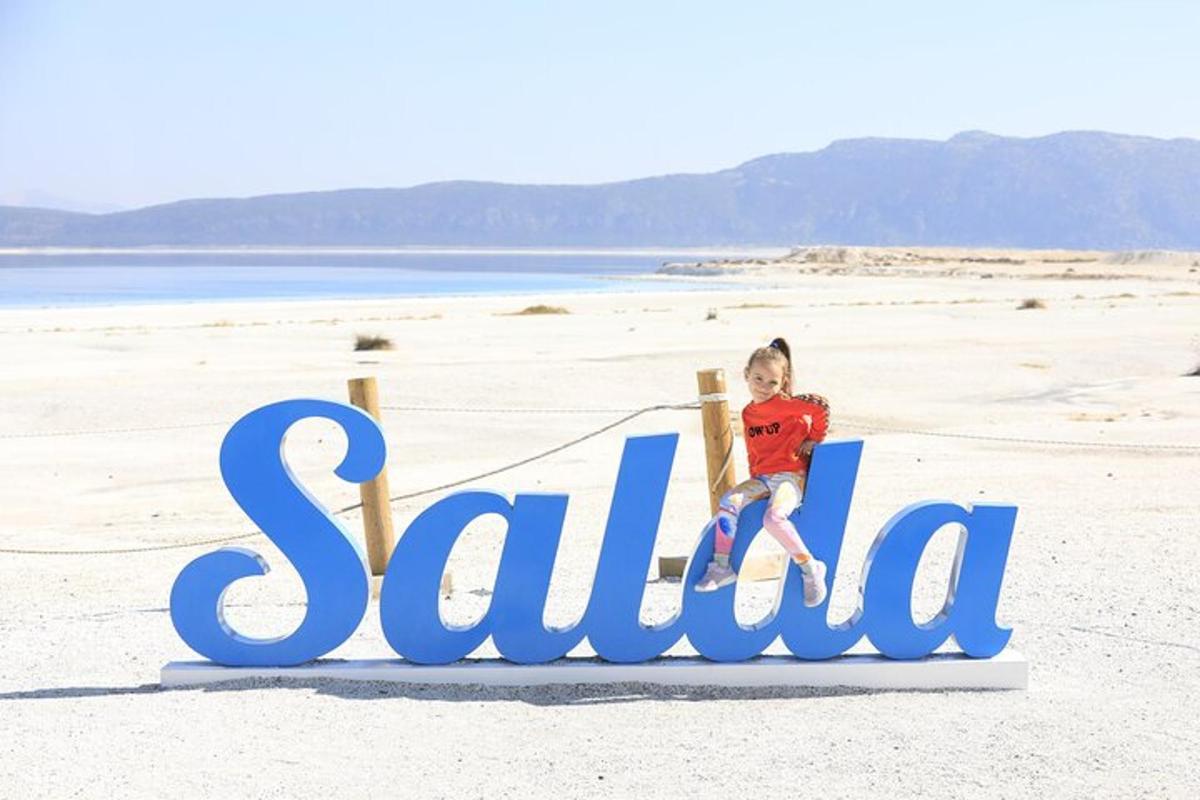 a little girl sitting on top of a sign on the beach